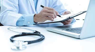 doctor-working-with-laptop-computer-writing-paperwork-